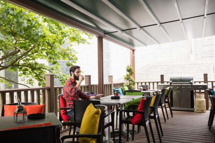 A covered deck with outdoor dining furniture, a gas grill, and a retractable awning surrounded by trees.