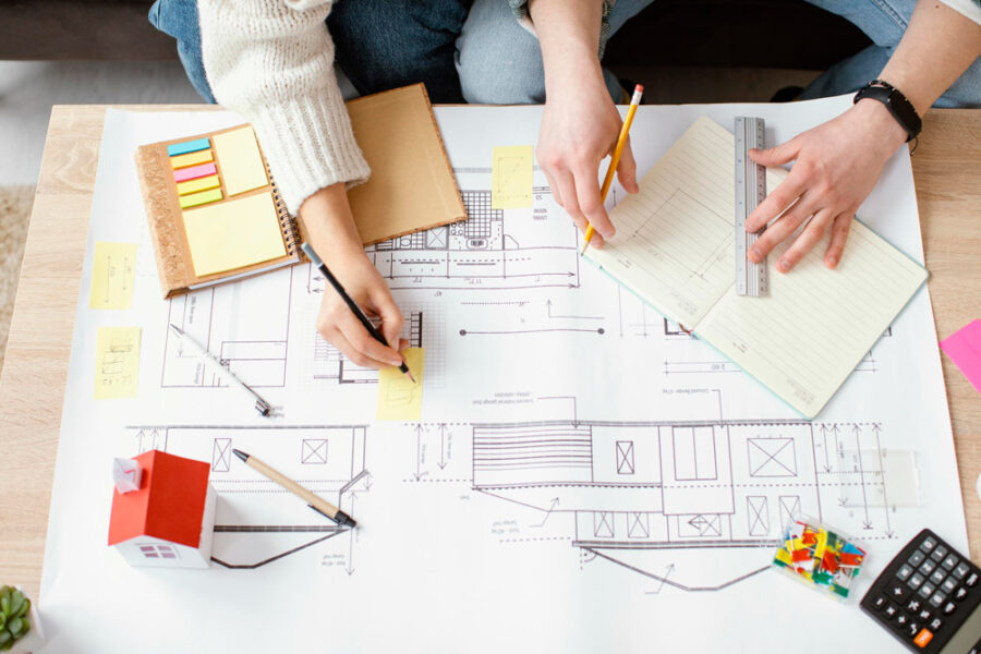 Two people reviewing and marking up home blueprints on a table during a remodeling planning session.