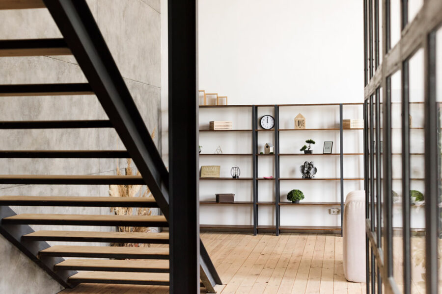 A modern interior with a floating wood and steel staircase next to an open metal shelving unit in a bright living space.