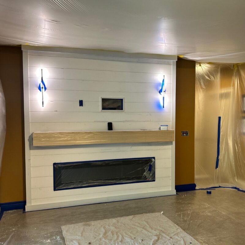 Freshly painted white shiplap accent wall with wood mantel and masked fireplace opening during basement renovation.