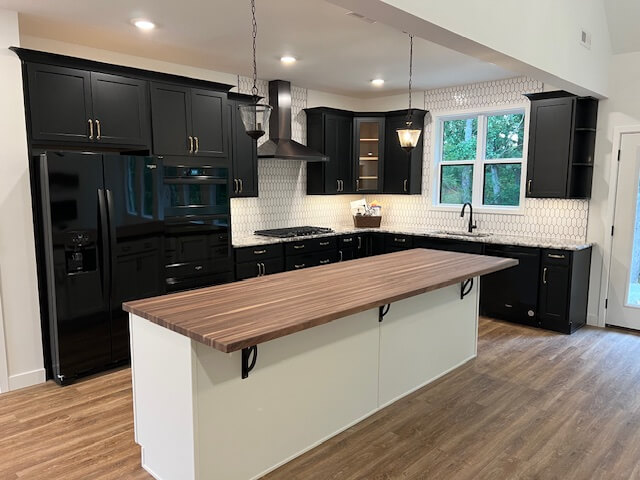Remodeled kitchen featuring black shaker cabinets, a butcher block island, hexagon tile backsplash, and hardwood floors completed by Nova Construction and Remodeling.